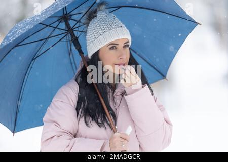 Magnifique brunette met sur le baume à lèvres vêtu de vêtements chauds à l'extérieur lors d'une journée froide d'hiver. Banque D'Images