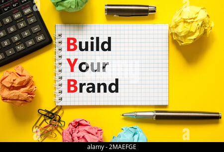 BYB construisez votre symbole de marque. Mots de concept BYB construisez votre marque sur une note blanche sur un magnifique fond jaune. Calculatrice. Business et BYB vous construisent Banque D'Images