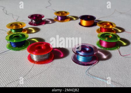 Gros plan d'un cercle de neuf fils multicolores sur cylindres en plastique semi-transparent multicolores appelés Bobbins (utilisés dans les machines à coudre), avec Banque D'Images