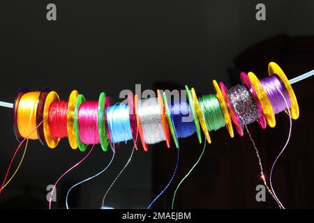 Gros plan d'une rangée de neuf fils multicolores sur cylindres en plastique semi-transparent multicolores appelés Bobbins (utilisés dans les machines à coudre). Banque D'Images