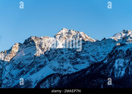 Soleil sur les pics de montagne abruptes couverts de neige en hiver, par une journée ensoleillée près du village de Guarda, en Suisse. Banque D'Images