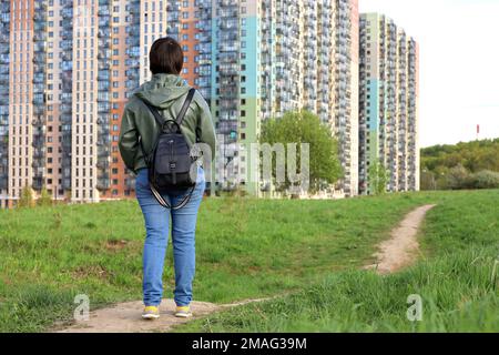 Femme sur pelouse verte regarde les nouveaux bâtiments, quartier résidentiel dans un secteur écologiquement propre. Industrie du bâtiment et concept immobilier Banque D'Images