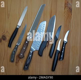 Huit couteaux de cuisine sur une planche en bois. Le premier est un couteau à tomates, le troisième un couteau à pain. Ensuite, un couteau japonais Gyuto. Banque D'Images
