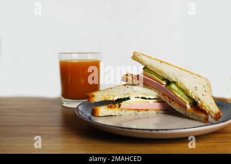 Petit déjeuner déjeuner déjeuner en-cas sandwich avec saucisse jambon fromage concombre verts se trouve sur une assiette à côté d'un verre de jus de pêche orange. Petit déjeuner européen Banque D'Images