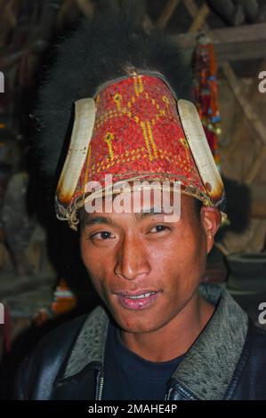 Mon, Nagaland, Inde - 03 02 2009 : Portrait intérieur du jeune homme de la tribu Naga Konyak portant un chapeau traditionnel de bambou rouge et de canne avec des défenses de sanglier et de la fourrure Banque D'Images