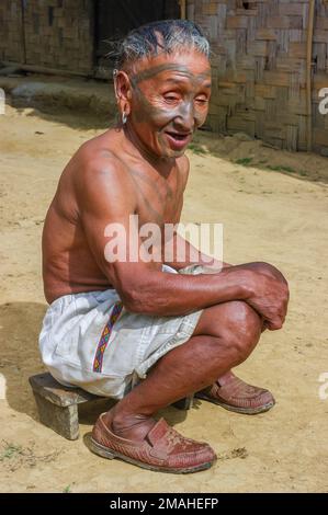 Mon, Nagaland, Inde - 11 20 2010 : Portrait du chasseur de tête de la vieille tribu Naga Konyak souriante, avec tatouage facial traditionnel assis à l'extérieur Banque D'Images