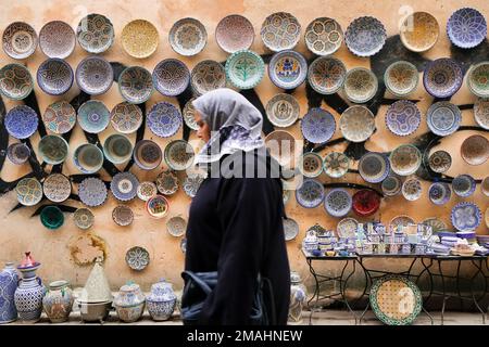 Fez, Maroc - image floue d'une femme musulmane locale couverte qui passe devant des produits en céramique à vendre sur le marché de Fes el Bali. Fond de déplacement horizontal de Fes. Banque D'Images
