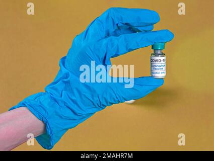 Main dans un gant de latex contenant un flacon en verre de vaccin contre le coronavirus Banque D'Images