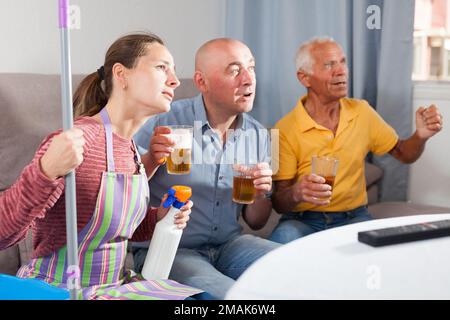 Femme assise pendant le nettoyage de la maison, mari et père regardant la télévision Banque D'Images