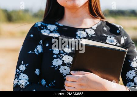 Fille chrétienne méconnaissable tenant une bible sous son bras dans le champ. Sola scriptura. Copier l'espace Banque D'Images