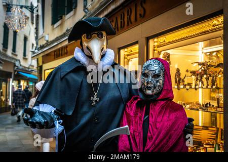 Un homme en costume de médecin de peste et une femme en costume de mort se tiennent dans une rue du soir à Venise, en Italie Banque D'Images