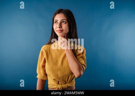 Jeune femme aux cheveux foncés sur fond bleu tenant sa gorge enflammée. Concept médical, mal de gorge. Avoir mal à la gorge, en tenant la main sur le cou, Banque D'Images