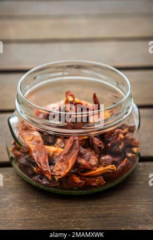 Un pot en verre transparent rempli de piments séchés chauds et déshydratés sur une surface en bois d'acacia Banque D'Images