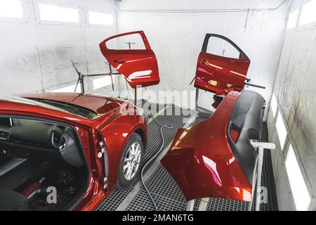 Une voiture rouge de luxe dans un atelier de peinture avec ses portes retirées pour une nouvelle couche de peinture. Photo de haute qualité Banque D'Images