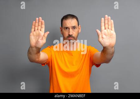 Homme hispanique barbu portant un t-shirt orange décontracté se détournant des mains montrant le rejet et le déni avec peur et l'expression dégoûtante. Arrêter et Banque D'Images