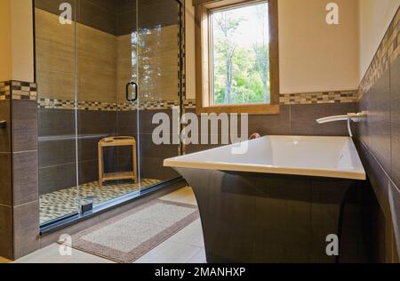 Chambre principale avec salle de bains attenante avec baignoire noire et blanche autoportante et cabine de douche en verre à l'intérieur d'une luxueuse maison scandinave en rondins et à ossature bois. Banque D'Images