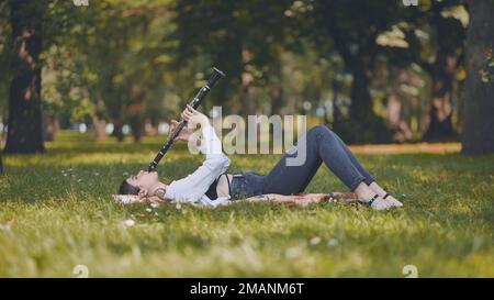 Une fille joue la clarinette en étant couché sur l'herbe dans le parc. Banque D'Images