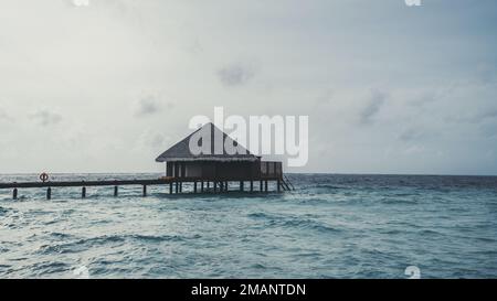 Une vue sur un bungalow sur l'eau avec un toit en pyramide, sur les eaux cristallines turquoise de l'eau de l'océan qui se lavent doucement au pont de l'l Banque D'Images