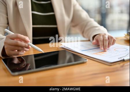 Une femme comptable professionnelle ou analyste financier utilisant une tablette numérique et examinant le rapport financier de l'entreprise à son bureau. rogné et gros plan i Banque D'Images