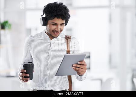 Sirotez un café tout en regardant ses amis. un jeune homme d'affaires portant un casque tout en utilisant une tablette numérique dans un bureau. Banque D'Images