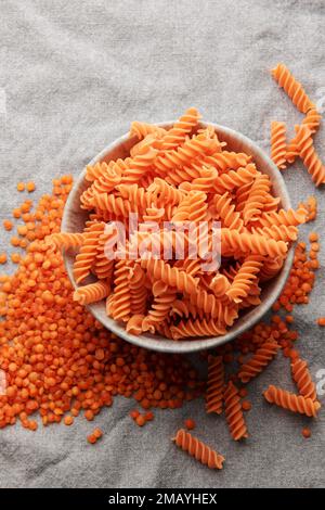 Pâtes de lentilles rouges fusilli sur fond textile gris. Bol avec pâtes crues et lentilles rouges. Pâtes sans gluten. Banque D'Images