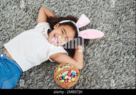 Trop le gagnant va le butin. Une jeune fille qui ponte sur le sol avec un panier d'œufs de Pâques à la maison. Banque D'Images