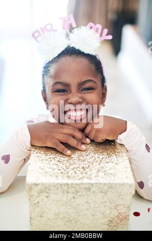 J'aime les cadeaux presque autant que j'aime les anniversaires. une petite fille tenant sur une boîte cadeau à son anniversaire. Banque D'Images