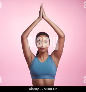 Je passe par ma routine de yoga. Portrait court d'une jeune femme attrayante et sportive méditant en studio sur fond rose. Banque D'Images