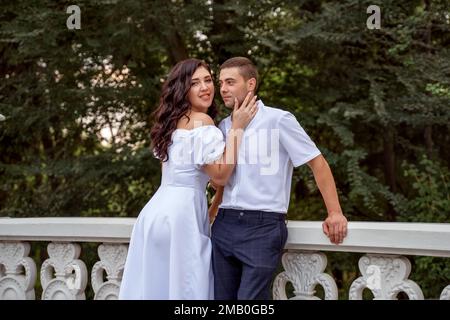 Belle fille à cheveux noirs touche doucement le visage de son mari avec sa paume. Jeune graine dans le parc par escalier en pierre pose le jour d'été. Banque D'Images