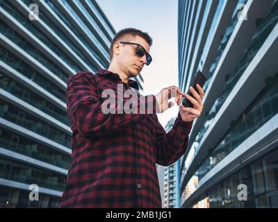 Jeune homme d'affaires étudiant travailleur utilisant le téléphone portable dans les mains dans les tours modernes de nouveau bâtiment bleu de bureau. Banque D'Images