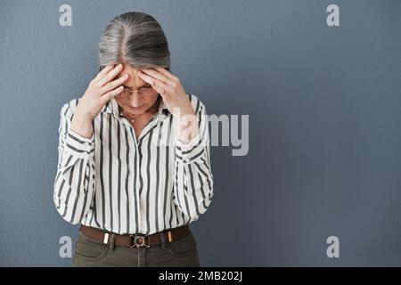 Le processus est stressé, le progrès sera le meilleur. une femme d'affaires mûre tenant sa tête souffrant d'un mal de tête intense contre un noir Banque D'Images