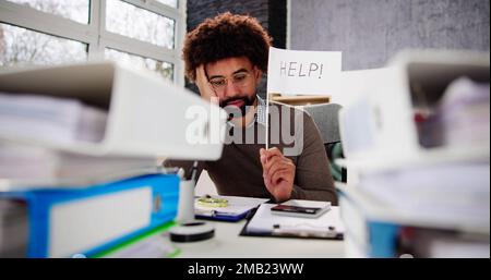 Sad Men in Office with Tax Workload and Paper Files Holding Help Flag Banque D'Images