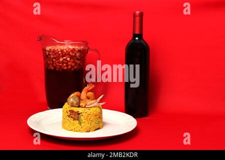 Paella riz avec fruits de mer traditionnel de Valence Espagne servi sur une plaque blanche à côté d'un pichet de clericot avec des fruits, une bouteille de vin rouge Banque D'Images