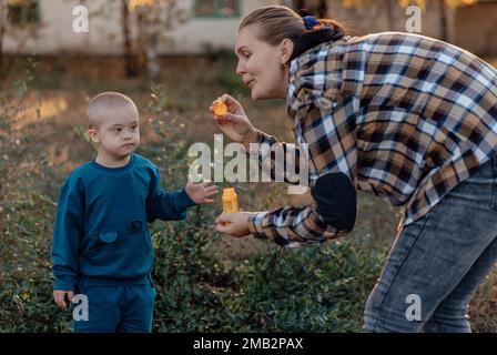 Un garçon, une personne atteinte du syndrome de Down, marche dans le parc avec sa mère, des bulles de savon Banque D'Images