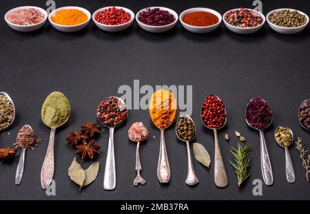 Composition composée de variations d'épices dans des bols blancs et des cuillères en métal sur un fond de béton foncé Banque D'Images