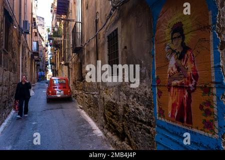 Ruelle étroite à Palerme avec grafficité, une Fiat rouge 500, balcons, linge suspendu et une femme marchant et utilisant un téléphone portable. Banque D'Images