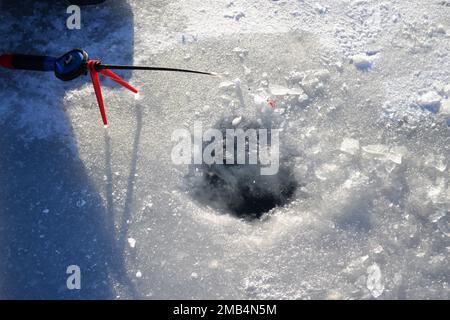 Pêche sous la glace en hiver. Pêcheur assis près d'un trou de glace et tenant une petite canne à pêche entre les mains. Pêche sous la glace en hiver. La petite canne à pêche se trouve près du trou dans la glace de la rivière le jour ensoleillé. En hiver Banque D'Images