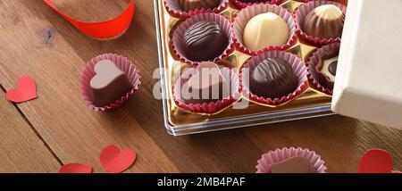 Présentation de l'assortiment de chocolats dans une boîte avec des découpes en forme de cœur rouge sur une table en bois rustique. Vue en hauteur. Banque D'Images
