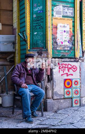 Un vendeur prend un repos et fume une cigarette devant son magasin sur un marché local. Banque D'Images