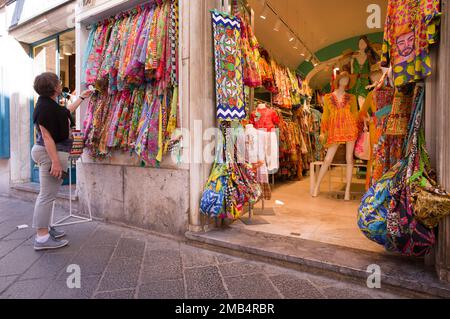 Femme plus âgée regardant et examinant des tissus et des robes typiquement siciliens, Corso Umberto, Taormina, Sicile, Italie Banque D'Images