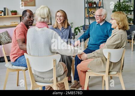 Groupe de personnes âgées heureuses assises sur des chaises et travaillant avec un psychologue à la thérapie dans une maison de soins infirmiers Banque D'Images