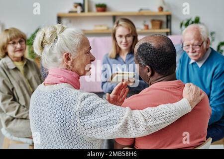 Vue arrière d'une femme âgée qui apprend à parler, elle est assise et parle à un homme afro-américain pendant la séance avec un psychologue Banque D'Images