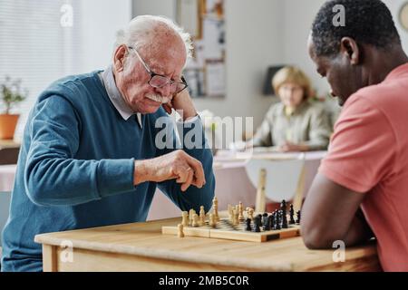 Les hommes âgés passent leur temps libre pour jouer aux échecs ensemble à table dans la maison de repos Banque D'Images