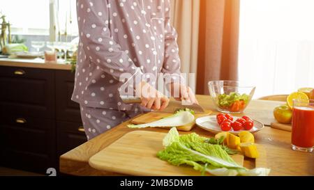 La femme de ménage enceinte hache le concombre pour la salade de légumes Banque D'Images