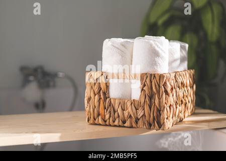 Serviettes de bain blanches roulées dans un panier en jute tissé sur une étagère en bois salle de bain rangement Banque D'Images