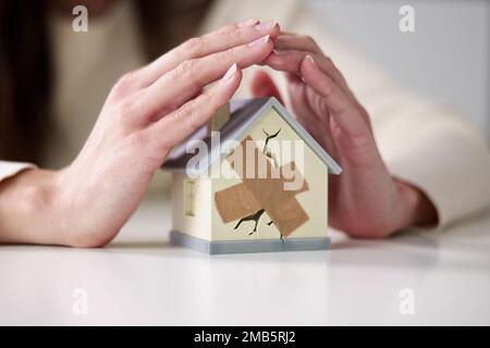 Femme d'affaires protégeant la maison brisée. Dommages immobiliers Banque D'Images