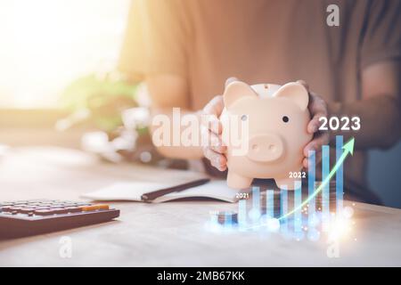 La banque de piggy avec l'homme calculant le revenu et le retour sur investissement en 2023. Économiser de l'argent la richesse et la finance ont augmenté. Affaires, finance, investissement, F Banque D'Images