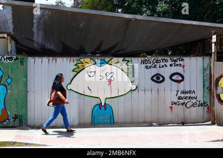 Femme qui passe devant une fresque pour protester contre le nombre de blessures aux yeux infligées par la police anti-émeute à des manifestants lors des manifestations chiliennes de 2019-2020, Copiapo, Región de Atacama, Chili. L'espagnol se traduit par : «cela nous a coûté tellement cher d'ouvrir les yeux, et maintenant ils veulent nous laisser aveugles». Banque D'Images