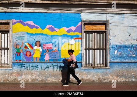Femme marchant devant une fresque murale sur le mur de l'école protestant contre la violence à l'égard des femmes et réclamant l'égalité des droits pour les femmes, Copiapo, Chili Banque D'Images