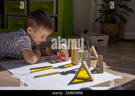 Un petit garçon mignon tire sur le sol de sa chambre. Cercles sur une feuille blanche les ombres des dinosaures projettent de la lumière du soleil. Banque D'Images